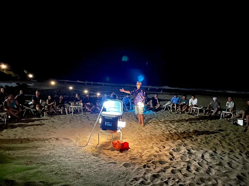 Team gathering on the beach at night with a speaker addressing the group