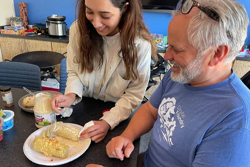 Colleagues sharing elote and laughing together in the office kitchen